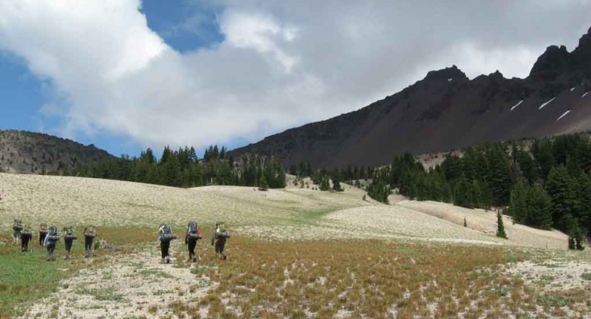 a group of students hike across an alpine meadow on an outward bound trip